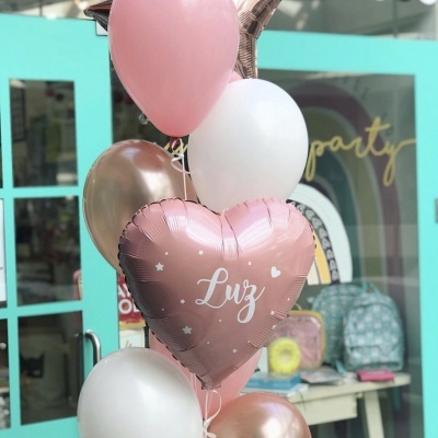 Balões decorativos em rosa, branco e dourado com a palavra 'Luz' num balão coração, junto a uma porta azul clara.