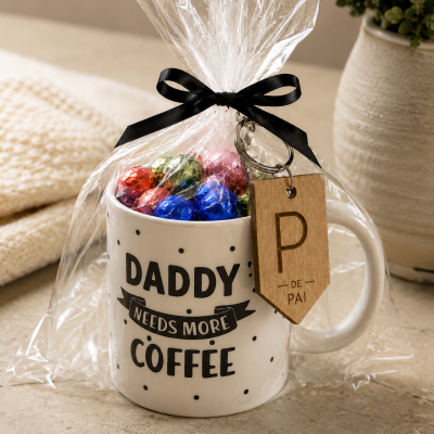 Caneca branca com texto e bombons coloridos embrulhada em celofane com laço preto e etiqueta de madeira