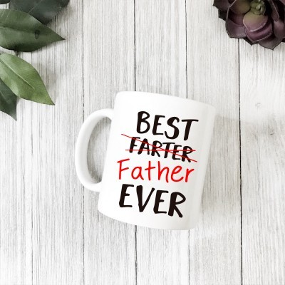 Caneca branca com texto 'BEST FARTEr Father EVER' em preto e vermelho sobre superfície de madeira clara