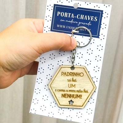 Porta-chave hexagonal de madeira com texto gravado a ser segurado por uma mão sobre cartão com padrão de pontos pretos e texto azul.