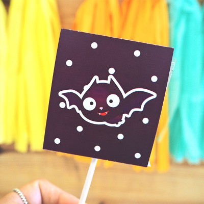 Balão quadrado preto com desenho de morcego branco cartoon e bolas brancas, fundo de roupas coloridas