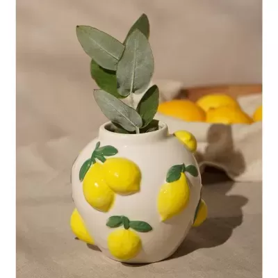 Jarro cerâmico branco com limões amarelos decorativos e ramo de folhas verdes.