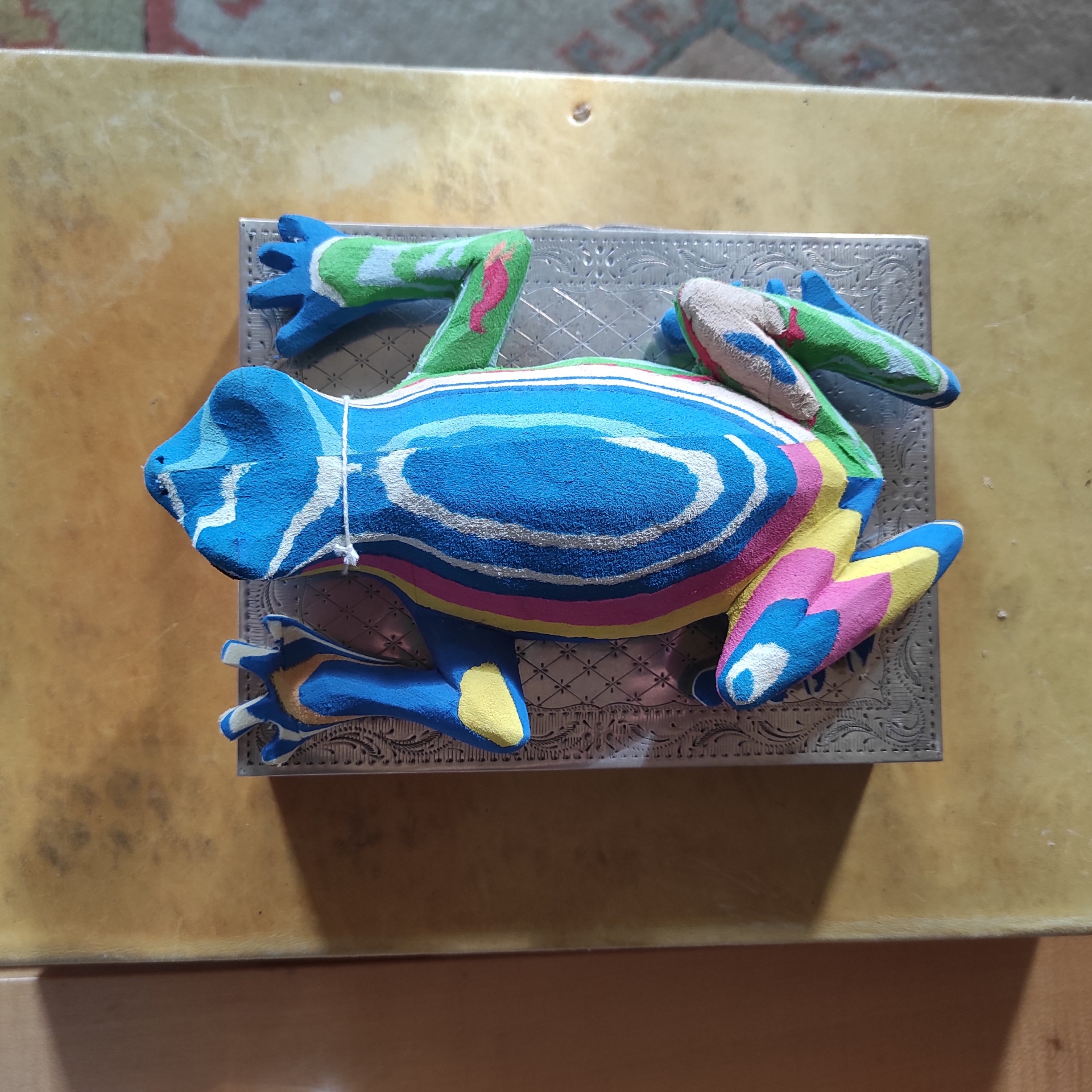 Sapo M Rã colorida em tecido sobre caixa cinzenta