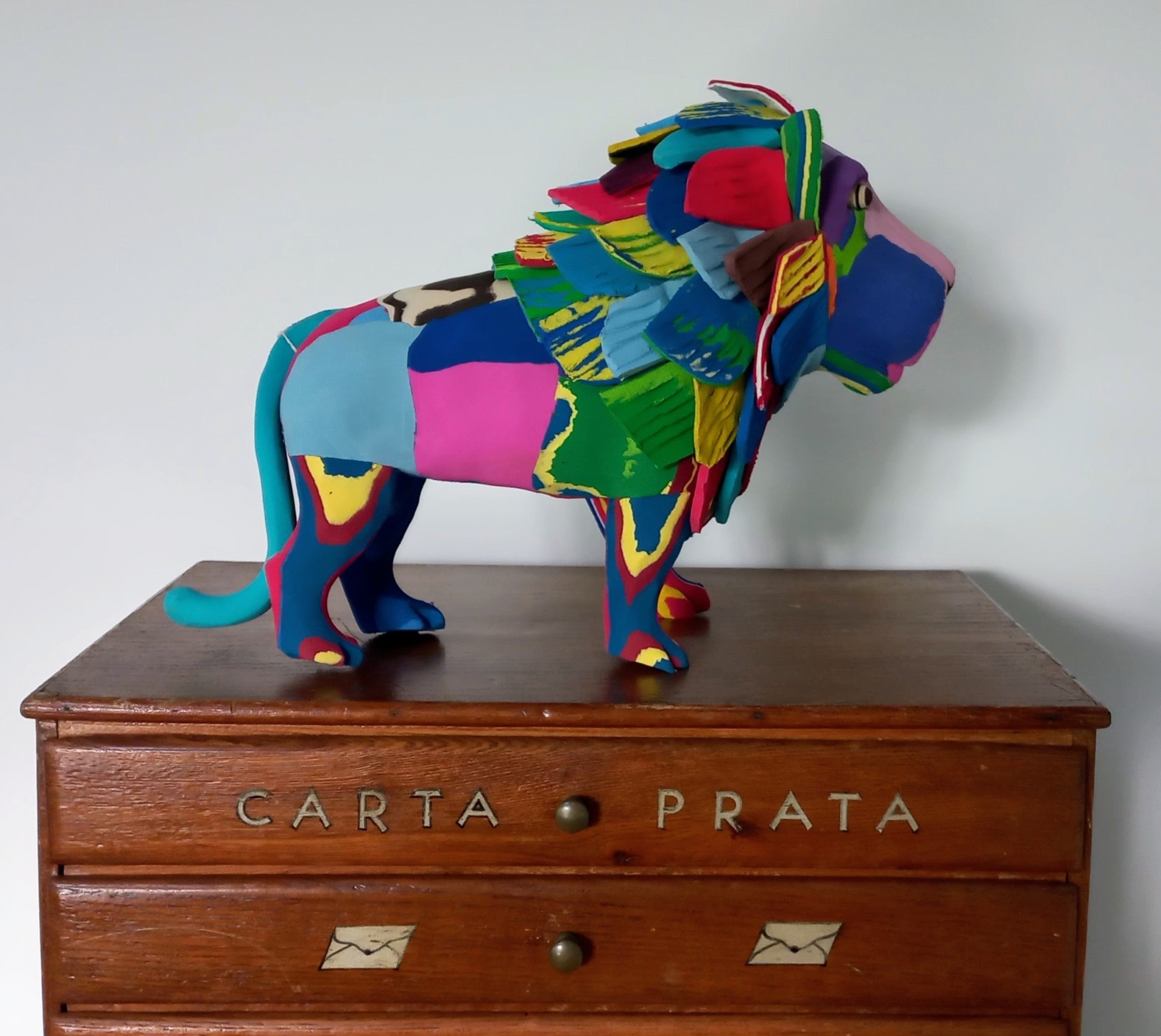 Leão L Estátua colorida de leão de tecido numa cómoda de madeira com inscrições