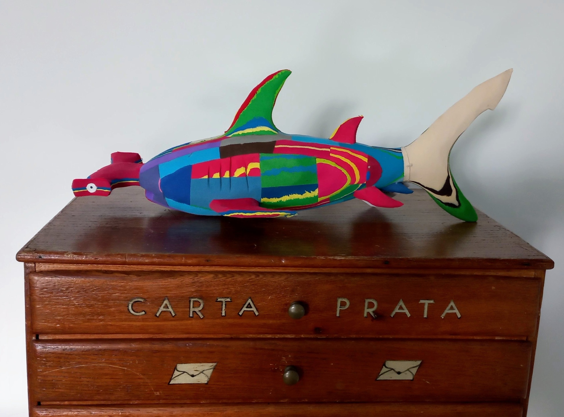 Tubarão Martelo M Escultura colorida de peixe sobre móvel de madeira com letras 'CARTA PRATA'