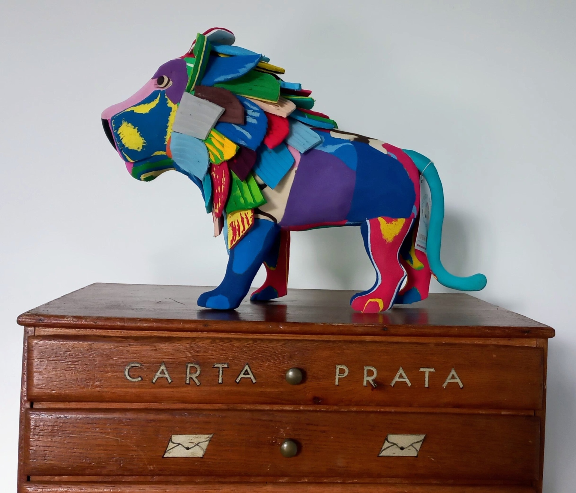 Leão L Estatueta colorida de leão sobre móvel de madeira com gavetas e inscrições