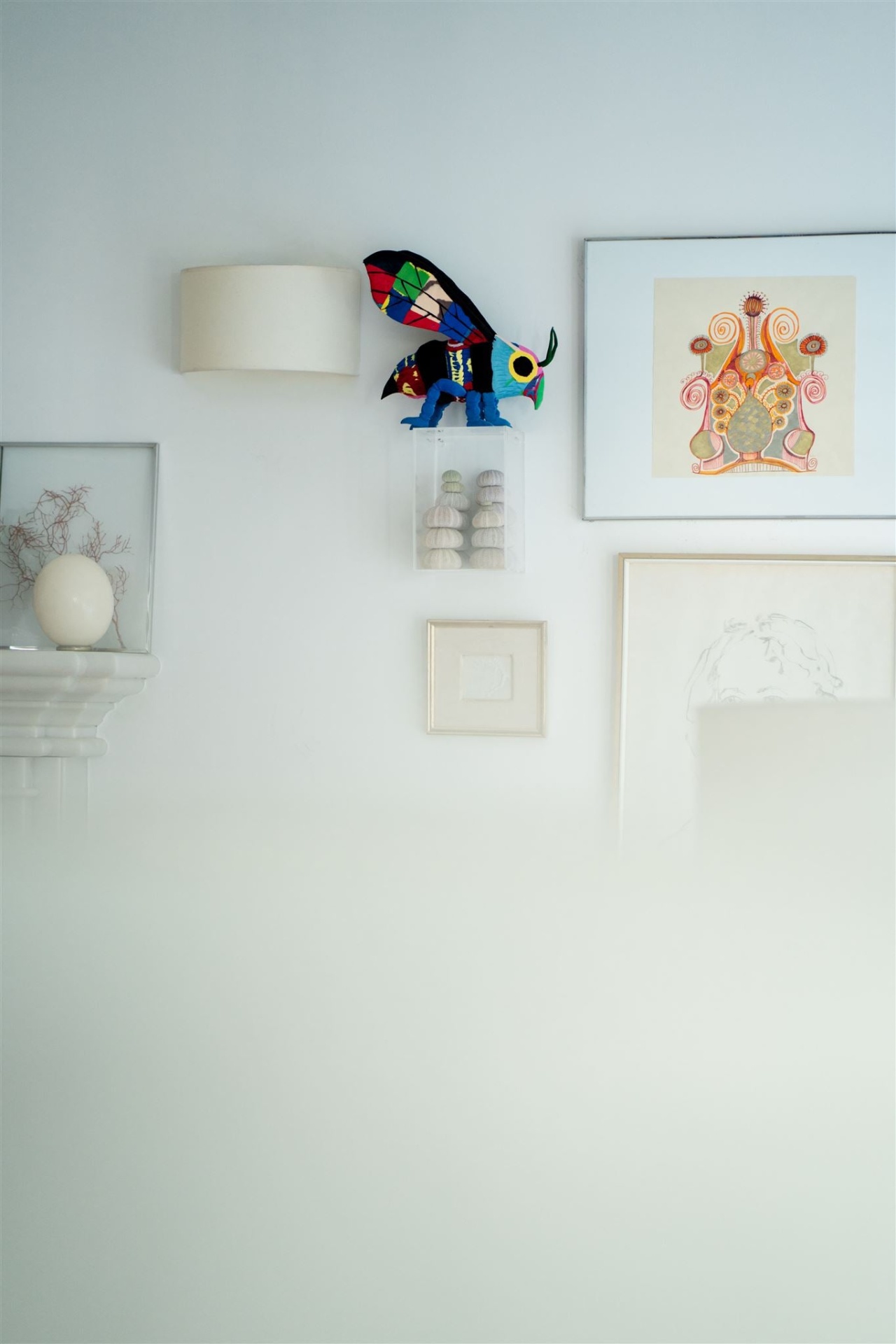 Abelha L Decoração de parede branca com abajur, inseto de tecido colorido, quadros e prateleira com objeto ovo branco