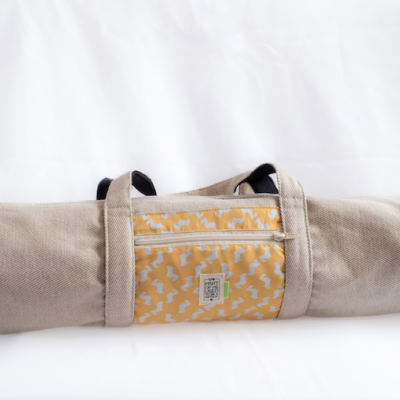 Saco de transporte em tecido bege com bolso estampado amarelo e branco e alças pretas.