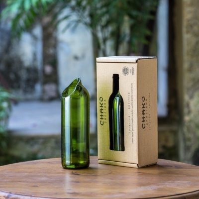 Garrafão de vidro reciclado verde com caixa de papelão numa mesa redonda de madeira ao ar livre