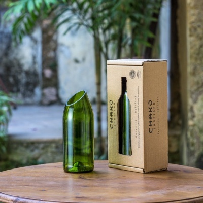 Garrafa verde de vidro inclinada ao lado da caixa de papelão castanha numa mesa redonda de madeira ao ar livre