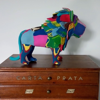 Estátua colorida de leão de tecido numa cómoda de madeira com inscrições