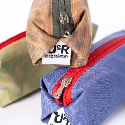 Três estojos de tecido coloridos com fechos de correr e etiquetas U2R United to Remake.