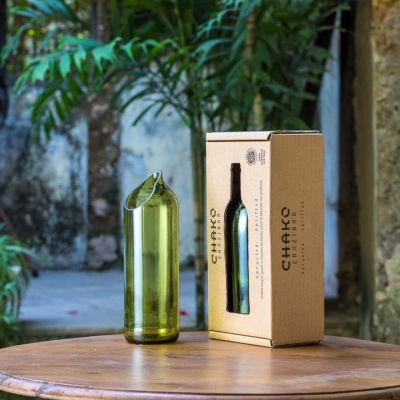 Garrafas de vidro verde com embalagem de cartão bege numa mesa de madeira exterior