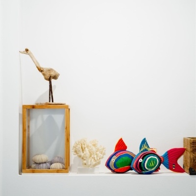 Prateleira branca com escultura de pássaro, suporte com ouriços-do-mar, coral branco e peixes de tecido coloridos