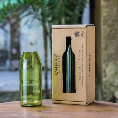Copo verde reciclado e caixa de cartão com garrafa verde e texto CHAKO numa mesa redonda de madeira