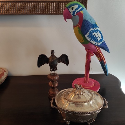 Mesa com escultura de pássaro metálica, papagaio colorido de tecido e caixa prateada decorativa