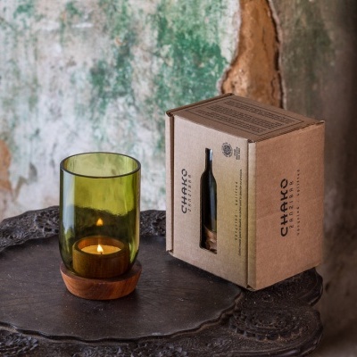 vela decorativa com vidro verde translúcido e embalagem de cartão reciclado sobre mesa antiga