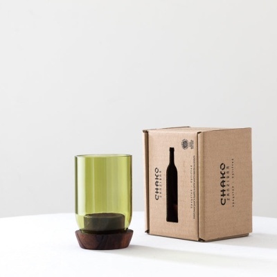 Copo de vidro verde com suporte de madeira e caixa de cartão castanha à direita