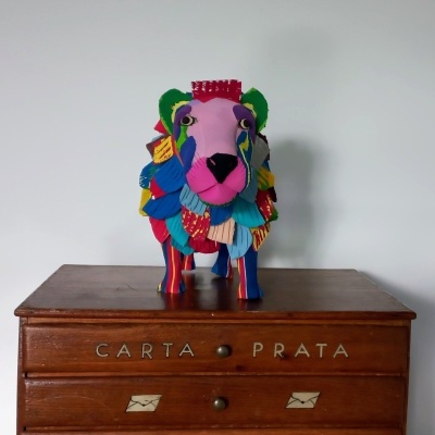 Estatueta colorida de animal em tecido sobre móvel de madeira com inscrição CARTA PRATA