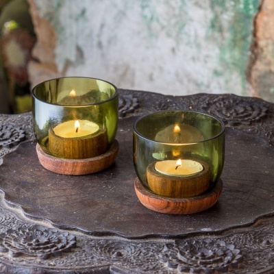 Dois porta-velas verdes em vidro com base de madeira sobre prato metálico decorativo
