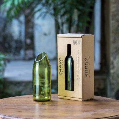 Vaso verde de vidro reciclado com embalagem de cartão 'CHAKO' numa mesa redonda de madeira ao ar livre