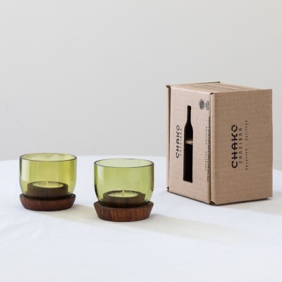 Dois copos verdes de vidro com bases de madeira em cima de superfície branca, ao lado de caixa de cartão castanho CHARKO.