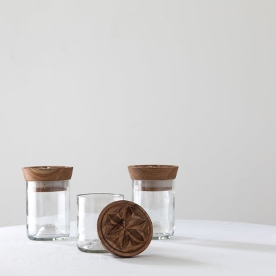 Três frascos de vidro transparentes com tampas de madeira sobre superfície branca