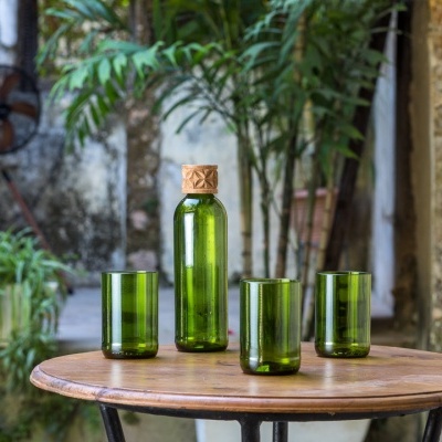 Conjunto de garrafa e três copos de vidro verde sobre mesa redonda de madeira