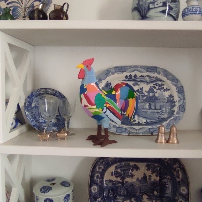 Estante com loiça azul e branca, galo decorativo colorido e saleiros prateados