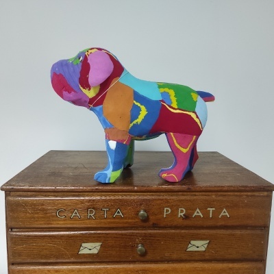 Estatueta de cão colorida em tecido patchwork sobre caixa de madeira com gavetas e inscrições 