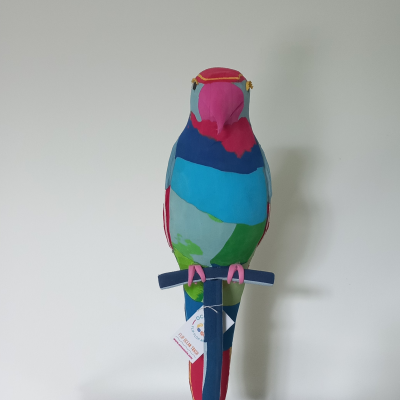 Estatueta colorida de papagaio em tecido sobre suporte azul e móvel de madeira
