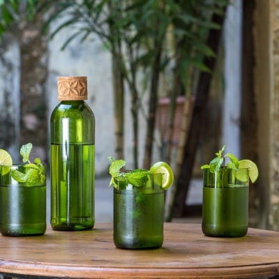 Garrafa verde e três copos com bebidas e decoração de hortelã e limão