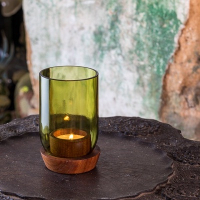 Vela em castiçal de vidro verde com base de madeira sobre superfície metálica escura