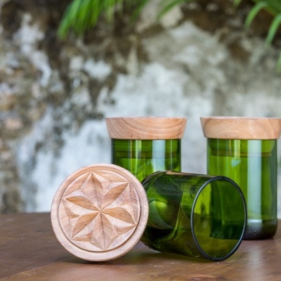 Três frascos de vidro verde com tampas de madeira e padrão gravado numa tampa sobre mesa de madeira