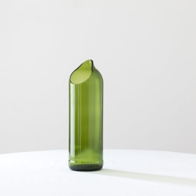 Frasco verde de vidro com abertura recortada sobre superfície branca