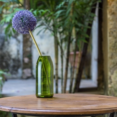 Vaso verde com flor roxa numa mesa de madeira em ambiente exterior