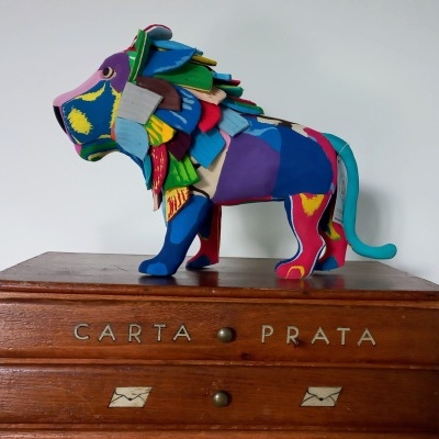 Estatueta colorida de leão sobre móvel de madeira com gavetas e inscrições