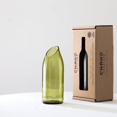 Garrafa verde reciclada com embalagem de cartão à direita, em fundo cinzento