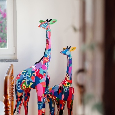 Esculturas de girafa coloridas em tecido com padrões abstratos, interiores com parede branca e janela