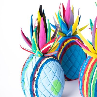 Três abacaxis decorativos de tecido colorido com folhas multicoloridas em fundo branco