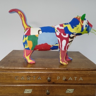 Escultura de cão colorida em tecido sobre caixa de madeira com letras e desenhos.