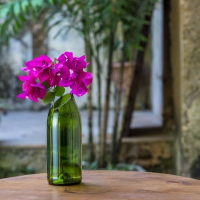 Vaso verde de vidro com flores cor-de-rosa numa mesa de madeira em ambiente exterior
