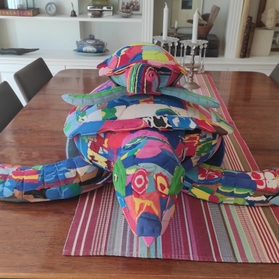 Escultura colorida em tecido de tartaruga sobre mesa de madeira com caminho listrado