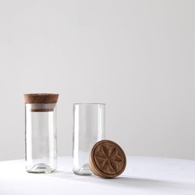 Dois jarros de vidro com tampa de cortiça, um aberto e outro fechado, sobre mesa branca