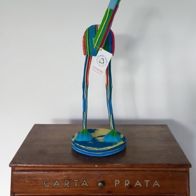 Escultura colorida de girafa em tecido sobre mesa de madeira com gavetas.