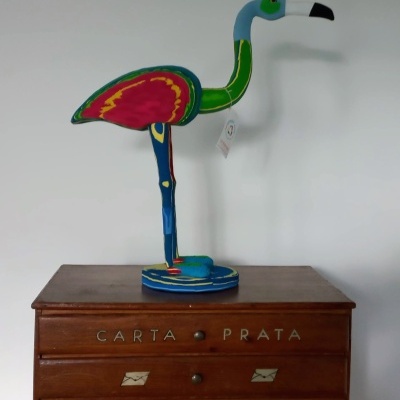 Escultura colorida de flamingo em madeira sobre cómoda de madeira com palavras CARTA PRATA