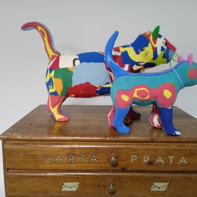 Duas esculturas coloridas de gato em tecido sobre móvel de madeira com palavras gravadas.