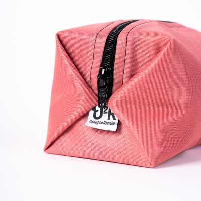 Estojo de tecido rosa com fecho preto e rótulo branco, em fundo branco.