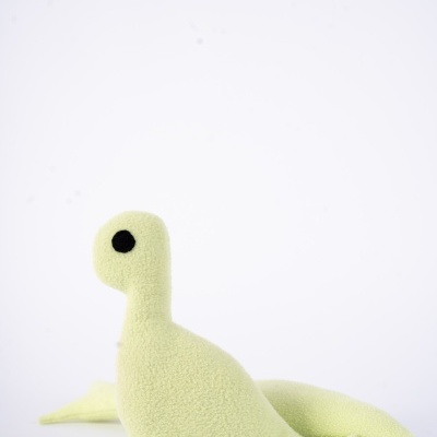 Pelúcia verde claro em forma de dinossauro com olhos pretos e textura macia