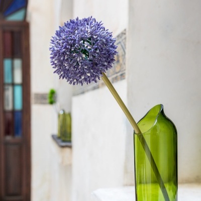 Flor lilás num vaso verde transparente sobre superfície branca
